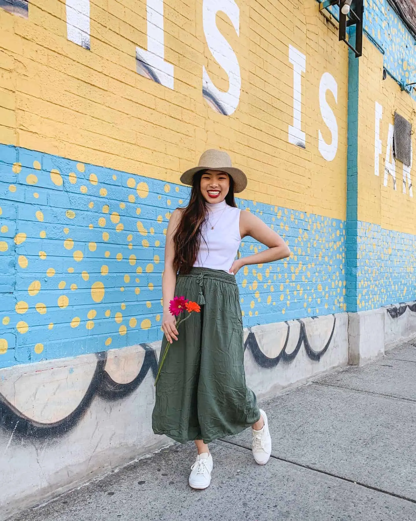 This is Paradise mural on Queen Street West in Toronto - wearing Aritzia straw hat, white sleeveless mock turtleneck, military green wide leg pants, Converse One Star sneakers