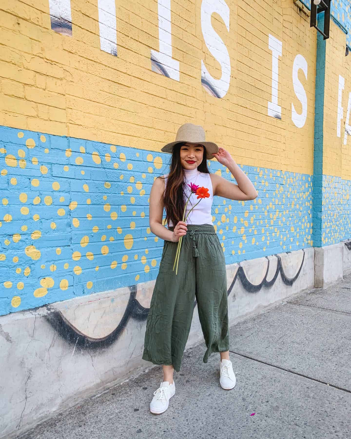 This is Paradise mural on Queen Street West in Toronto - wearing Aritzia straw hat, white sleeveless mock turtleneck, military green wide leg pants, Converse One Star sneakers