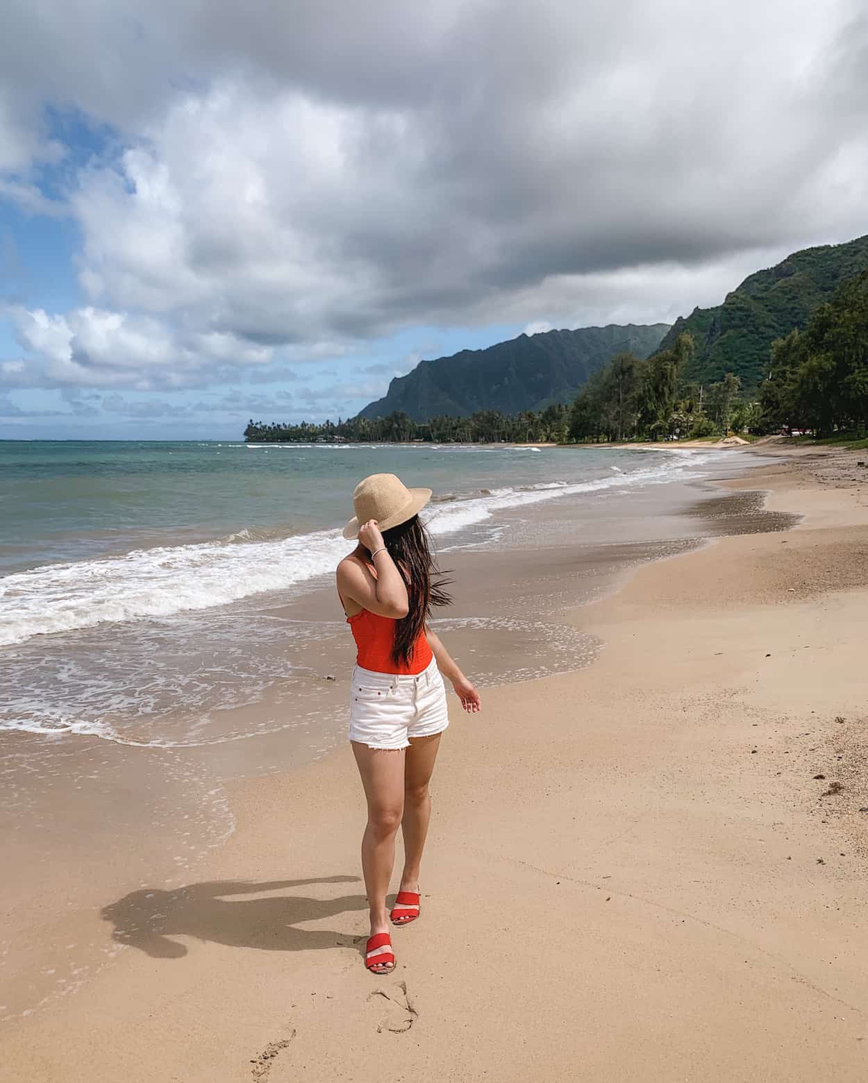 Hawaii vacation outfit featuring straw hat, red one piece swimsuit, white denim shorts, and red slide sandals