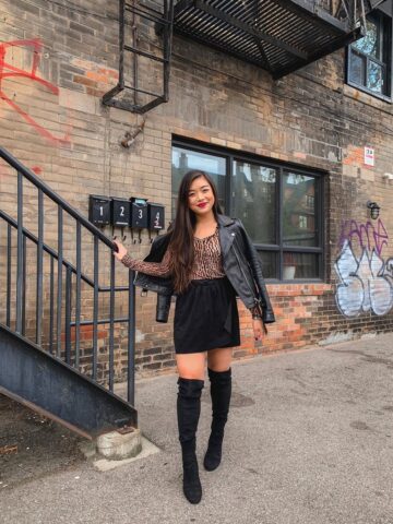 Casual fall outfit featuring leather moto jacket, leopard long sleeve top, black suede miniskirt, over-the-knee boots in Little Italy, Toronto