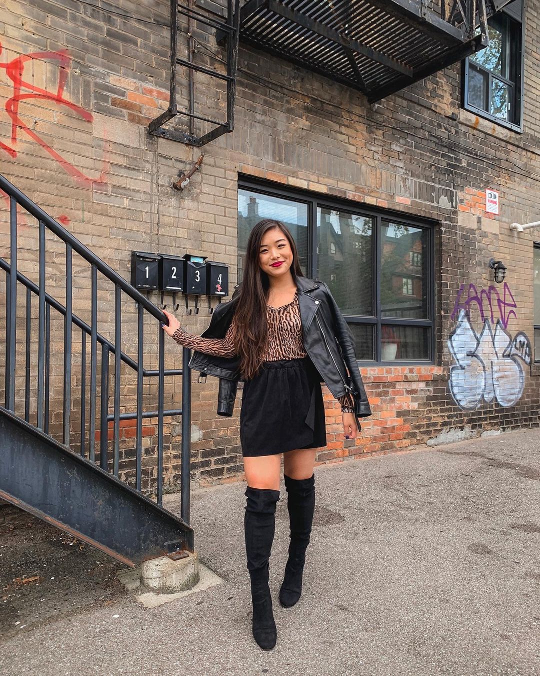Casual fall outfit featuring leather moto jacket, leopard long sleeve top, black suede miniskirt, over-the-knee boots in Little Italy, Toronto