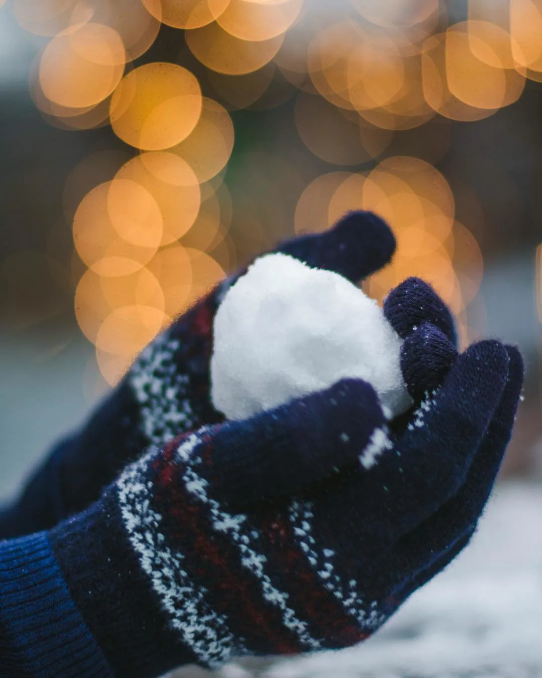 Holding snowball with MUJI winter gloves against holiday lights